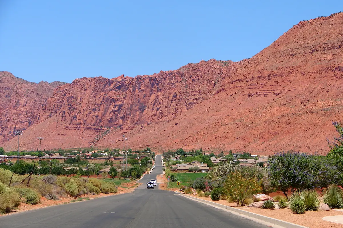 A residential street in Ivins, Utah, running toward a wall of red sandstone cliffs.