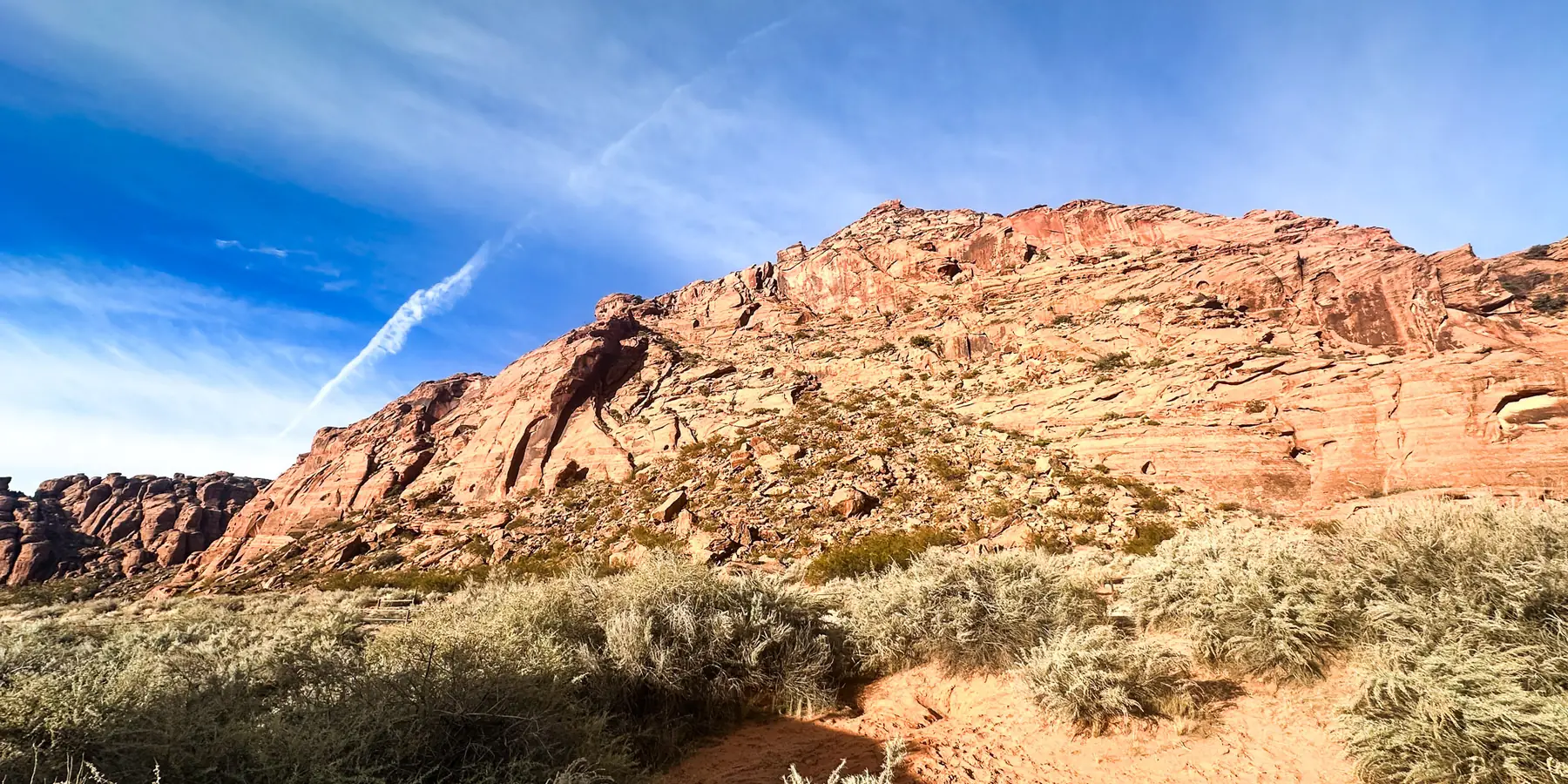 Morning sun on a red sandstone hill above golden grass and a sandy trail in Snow Canyon State Park.