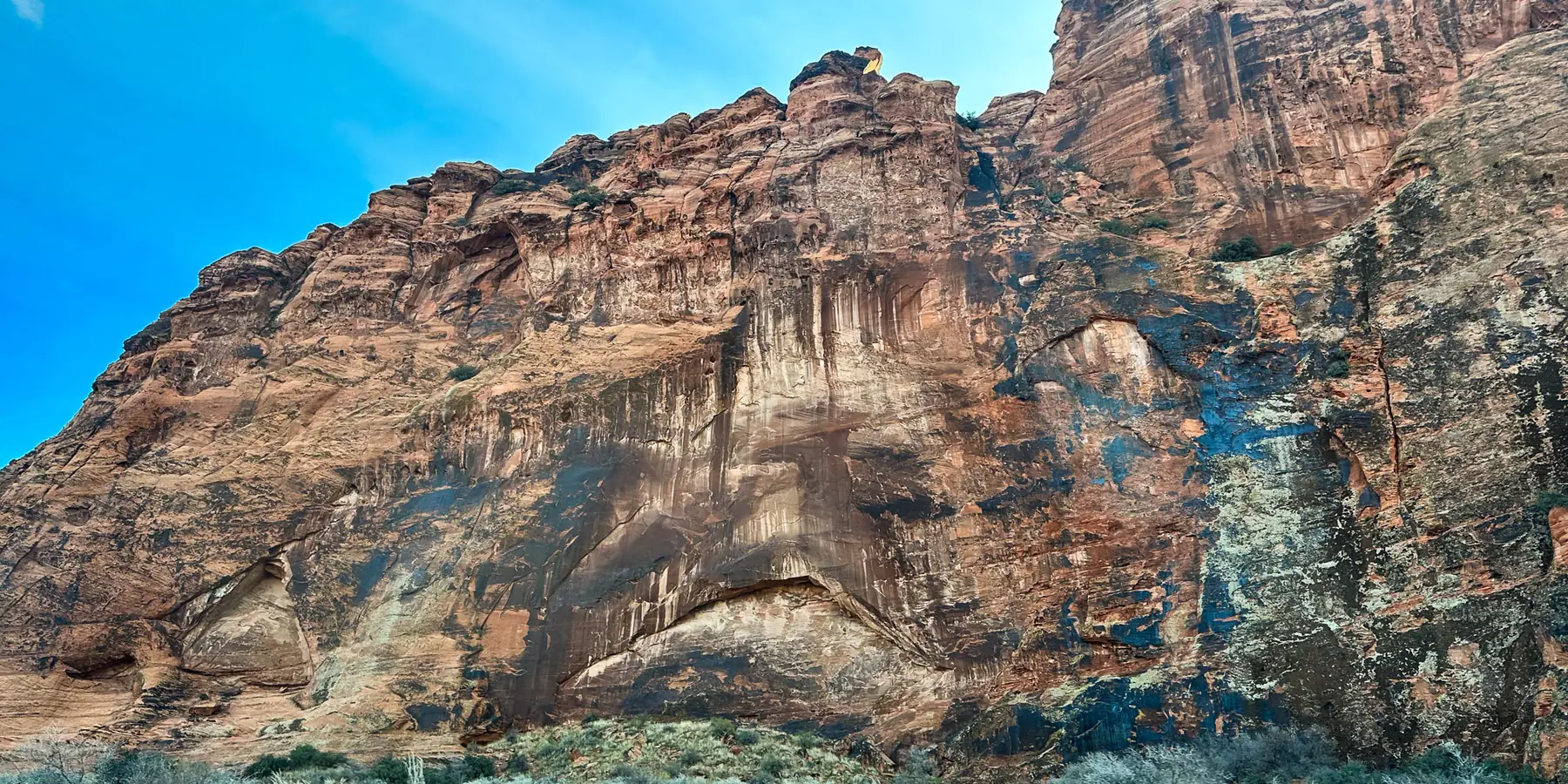 A tall streaked red-and-white sandstone cliff above pale shrubs in Snow Canyon State Park.