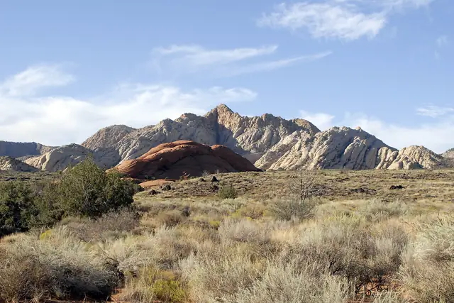 Grassy desert below jagged white and red sandstone peaks in evening light, Snow Canyon State Park.