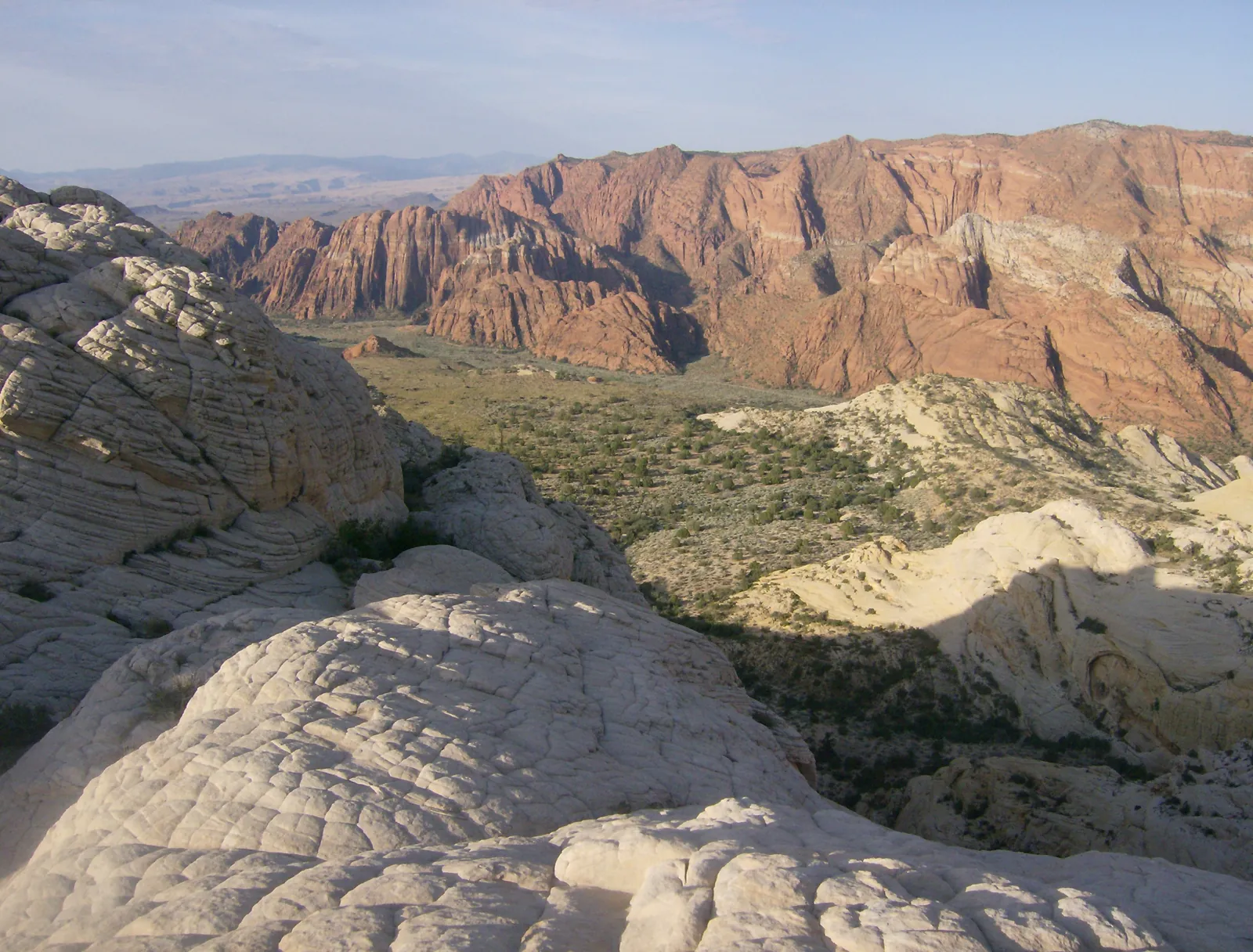 Rounded white sandstone in the foreground with red cliffs and a green canyon floor beyond, Snow Canyon State Park.